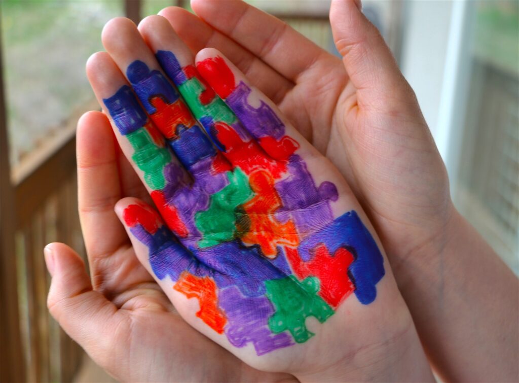 Mother holding hand of child with Autism puzzle pieces colored on palm of child's hand.