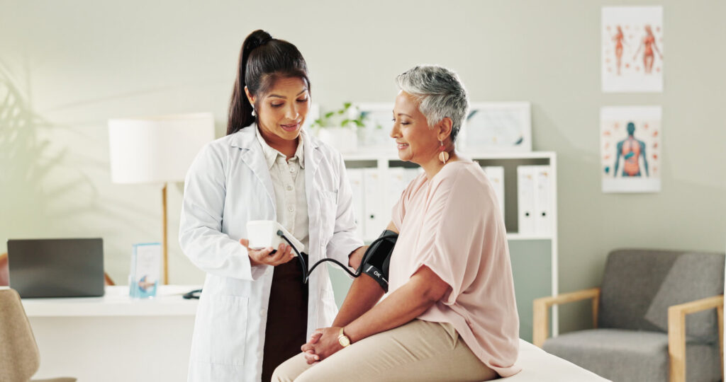 Female healthcare provider checking an older woman’s blood pressure during a routine wellness exam in a medical office