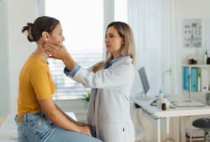 A female primary care doctor examining lymp nodes on neck of the teenage girl.