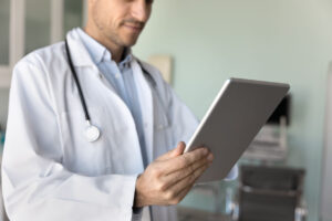 Male primary care doctor in white coat using modern technology.